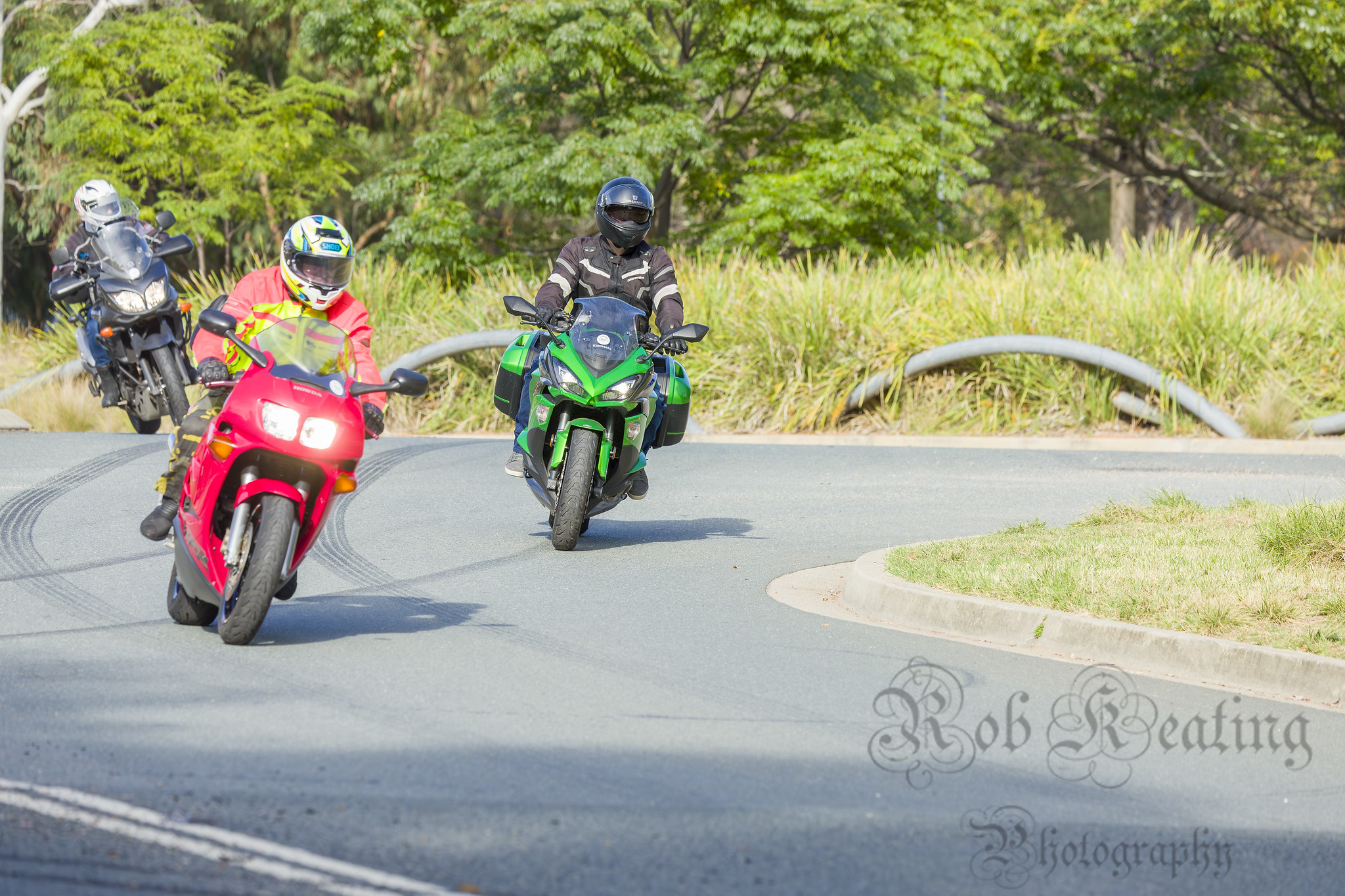 Three motorcycles taking a corner at low speed, a red Honda with a rider in high-vis gear, a lime green Kawasaki Ninja 100 with the rider in black gear and a blue Yamaha XT1200 with a rider in a black jacket and white helmet.
